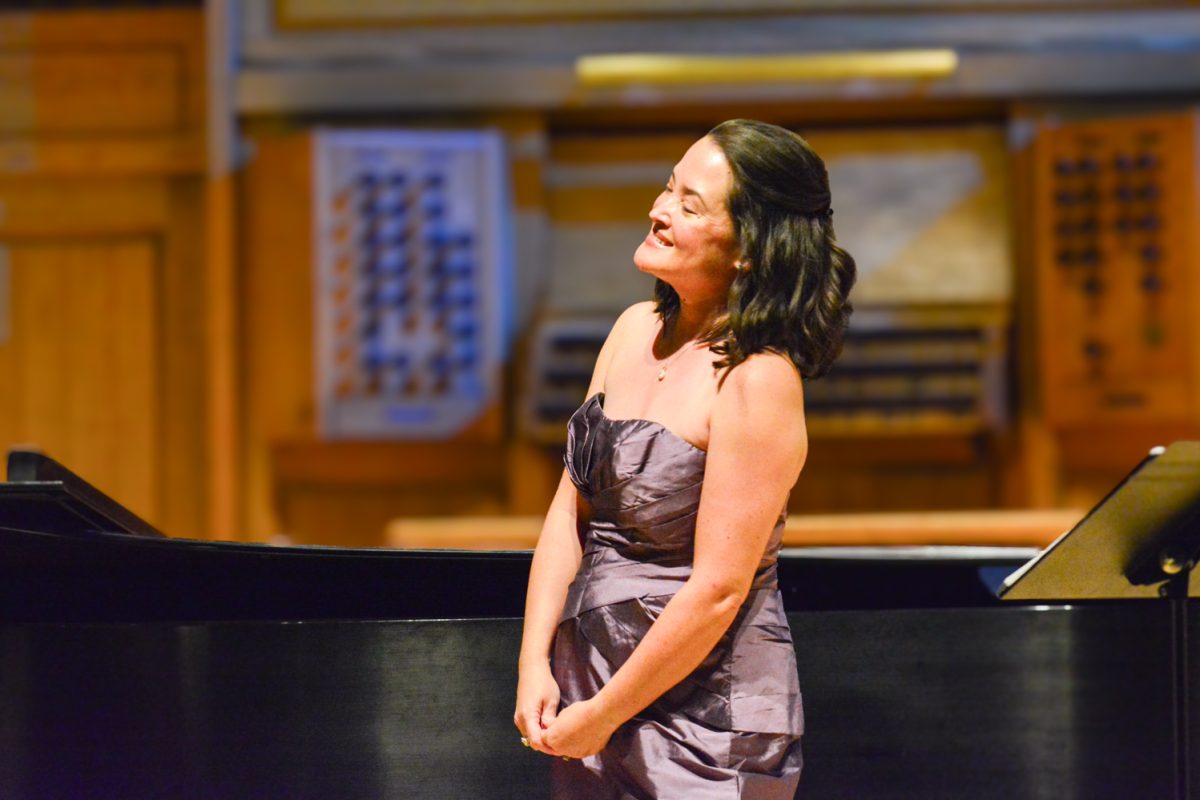 A woman in a purple dress smiling to the crowd after her performance.