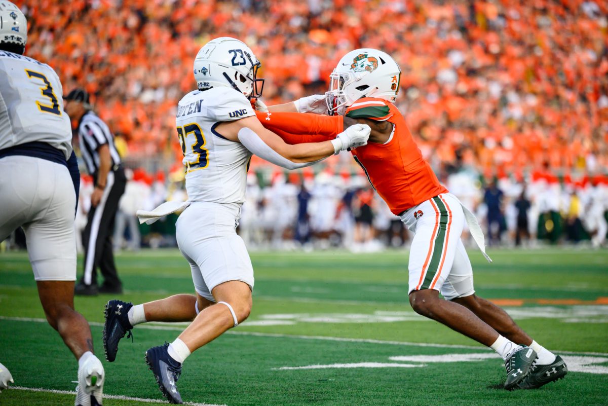 A football player in all white pushes a player in orange and white.