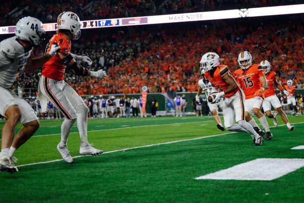 A football player in orange and white catches and runs with a ball while other players watch.