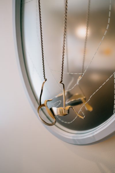A metal art piece handing from a chain against a frosted mirror.