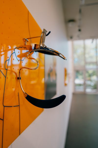A metal and plastic art piece attached to an orange pegboard showing a hand on a person's left shoulder.