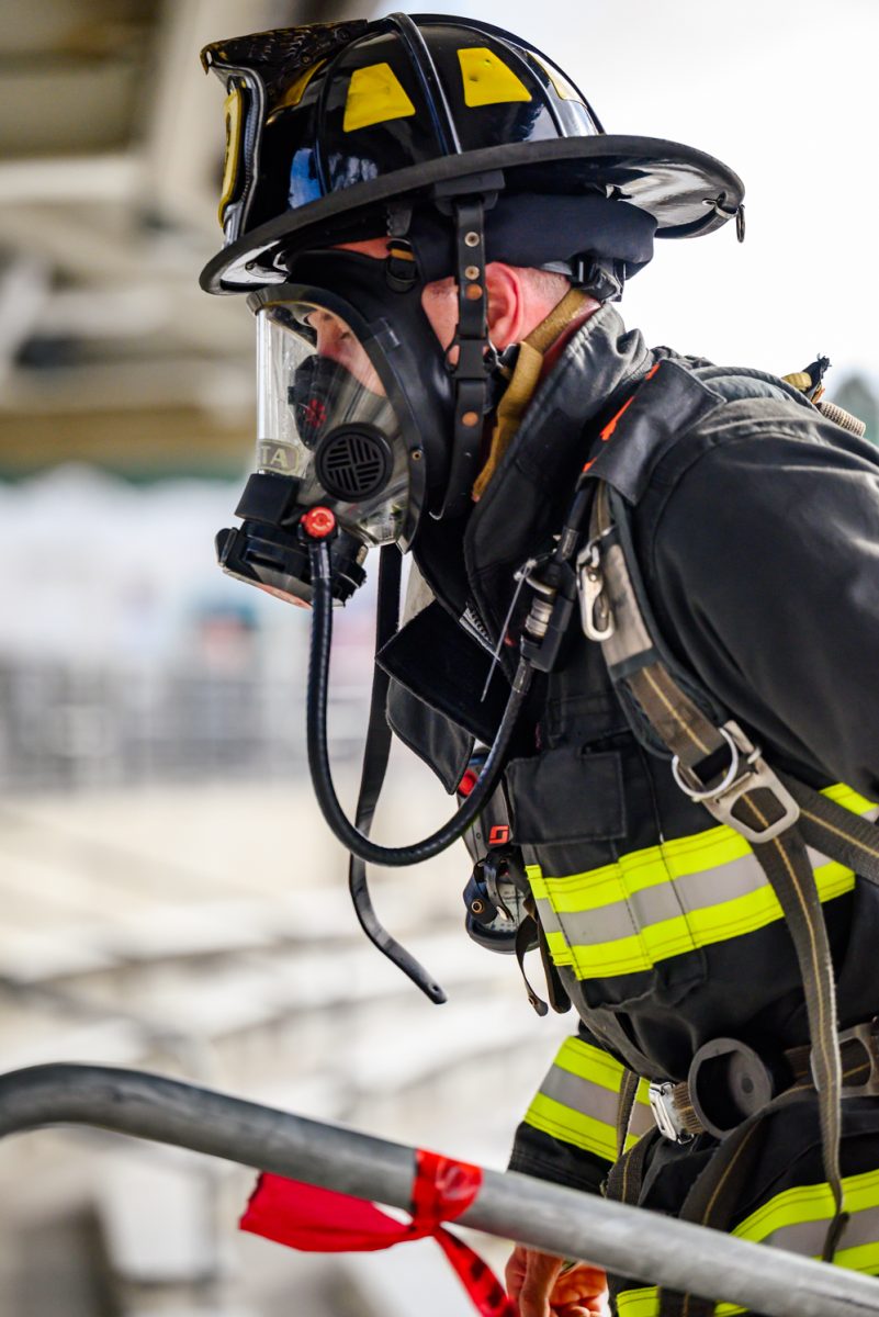 A male firefighter in full gear walks up a staircase. A large respirator covers his face.