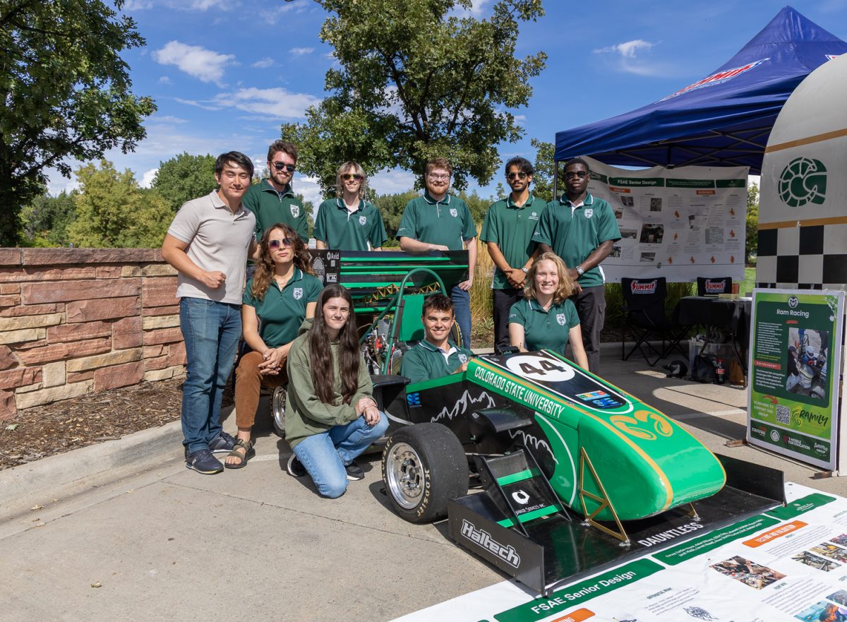 A group of people sit around their formula SAE car.