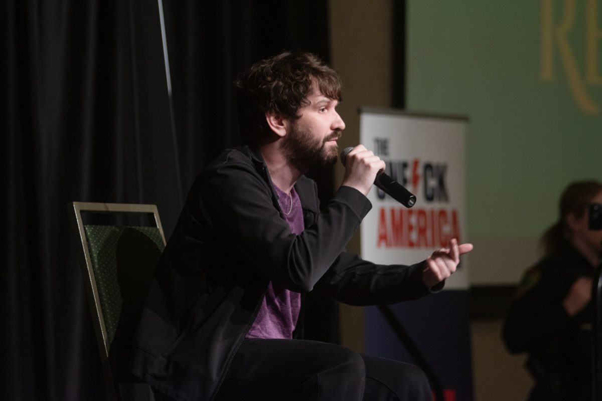 A young man is speaking into a microphone and pointing his finger outwardly.