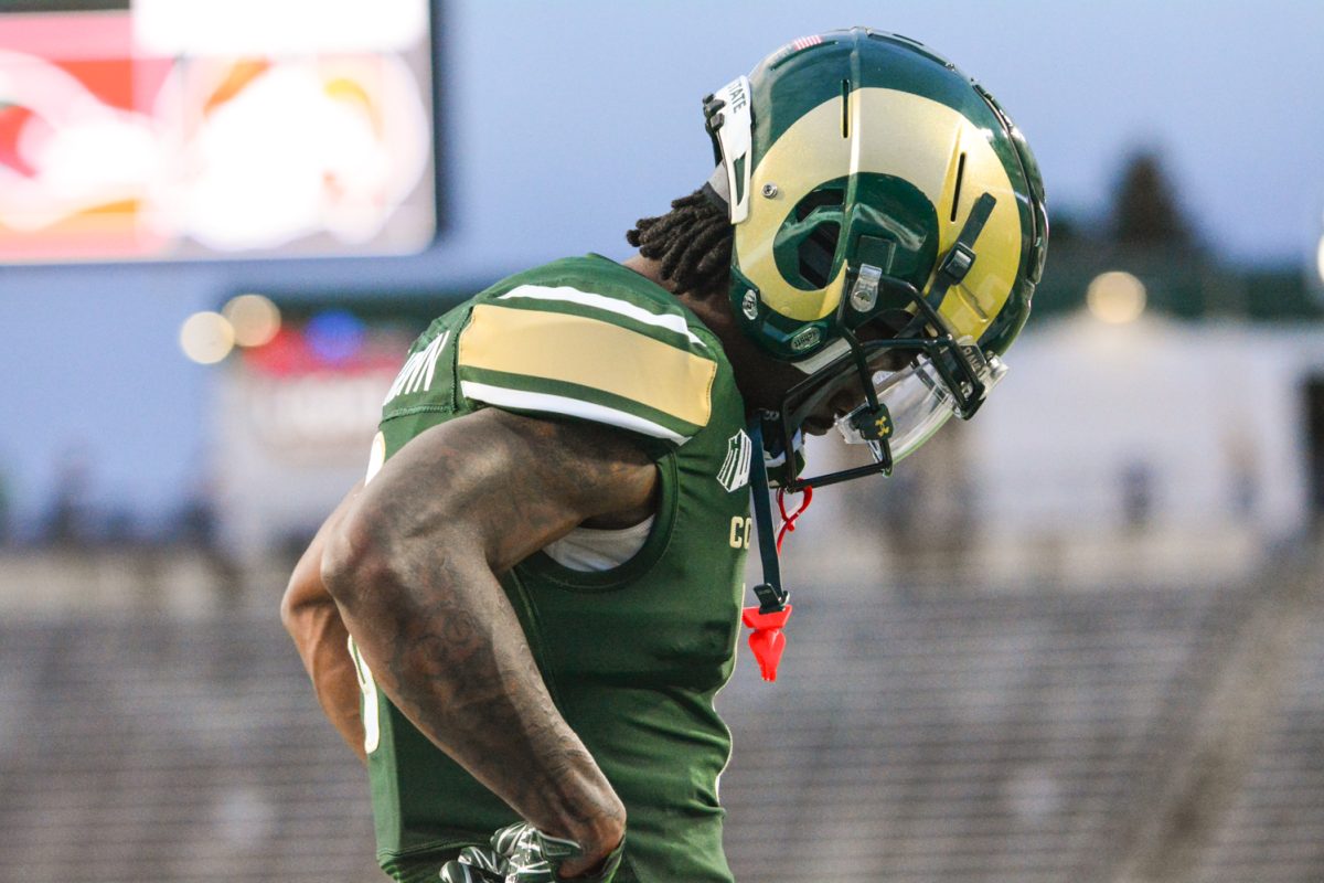 Football player in a green and gold jersey looks at the ground.