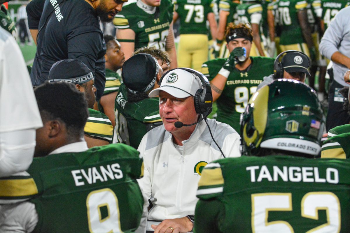 Football players in green and gold jerseys surround their coach in a white shirt.
