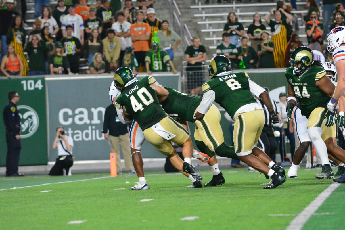 A player in a green and gold jersey tackling a player in a white, orange and blue jersey.