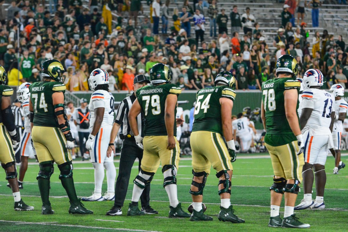 Four football players in green and gold jerseys lining up for the next play.