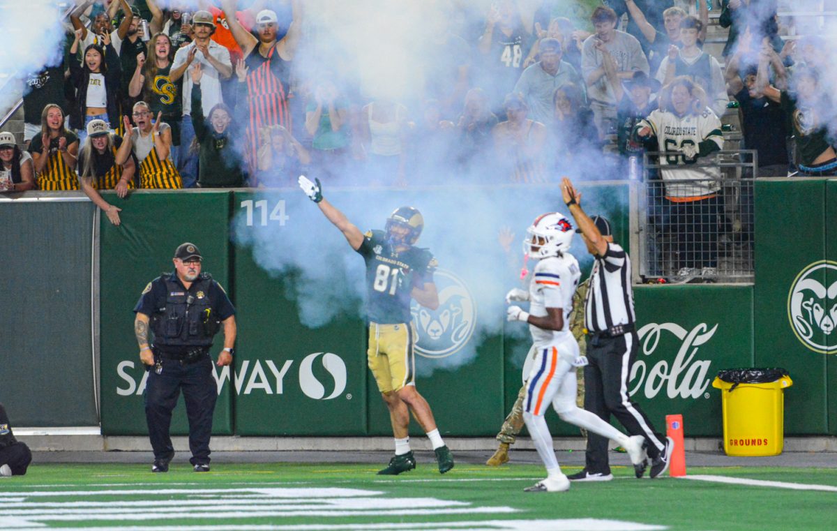 Football player in a green and gold jersey holding his hand up in a cloud of smoke.