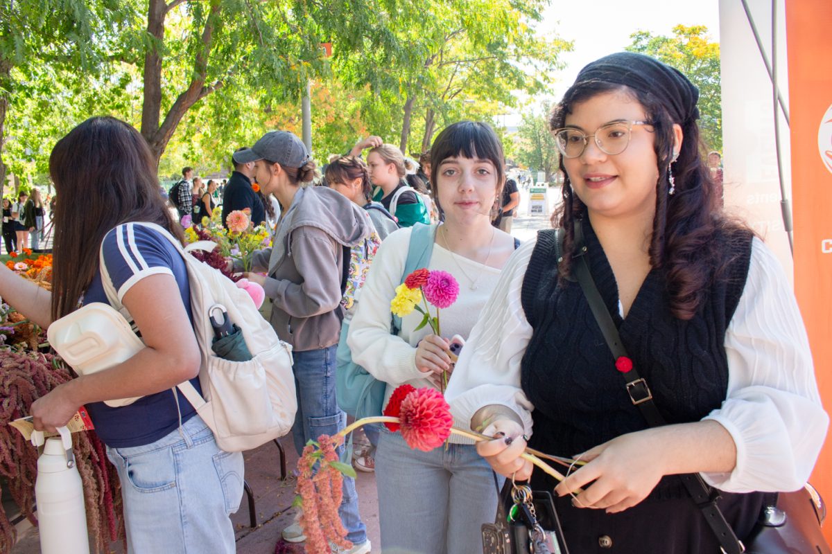 Colorado State University fourth-year English major Serena Torres carries a handful of vibrant flowers, alongside CSU first-year psychology major Madison Herron, while visiting the Feria de Flores event on The Plaza Sept. 24. Feria de Flores is an event celebrating National Latinx/é Heritage Month for CSU students to make bouquets of flowers.