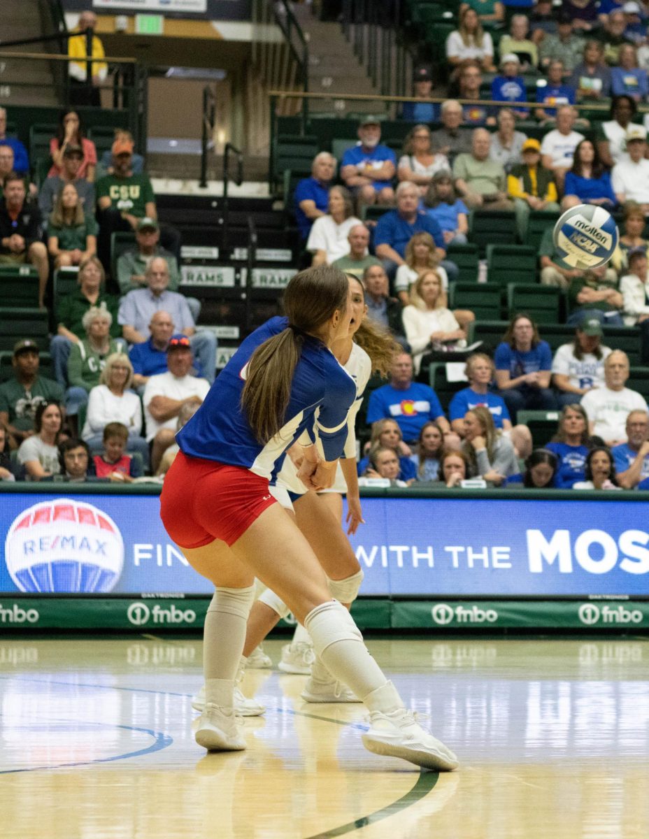 A women in a blue jersey and red shorts clasps her hands together in front of her body.