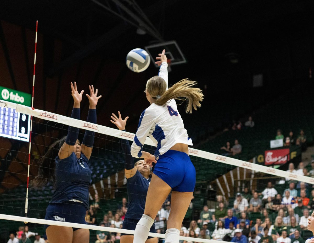A women wearing a white jersey and blue shorts jumps with her hand extended out towards the ball over the net.