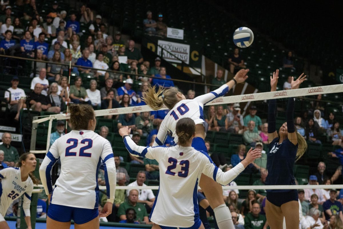 A women in a white jersey and blue shorts jumps and extends her hand over the net at the ball.