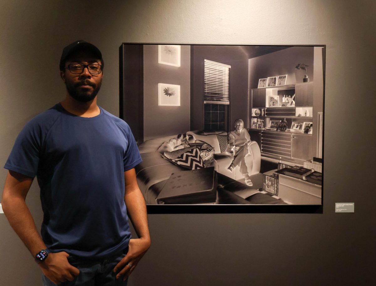 Justin Carney stands next to photograph 'Aunt Sonya with Family Photos' taken in his hometown Baltimore, Maryland as apart of his 'Full of Dreams' exhibition on Sept. 2nd in CSU's Directions Gallery. 