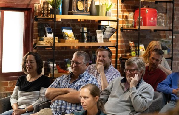 An older women wearing a black and grey long-sleeved shirt sits next to an older man wearing glasses with a blue collared shirt and another man wearing a grey sweatshirt and glasses.