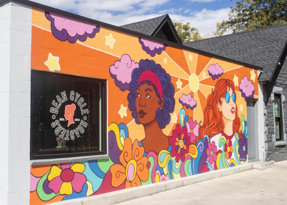 A colorful mural of two women, one with black curly hair and the other with long flowing red hair. There is a sun behind the both of them with rays extending over the whole wall, in addition to purple clouds behind them as well.