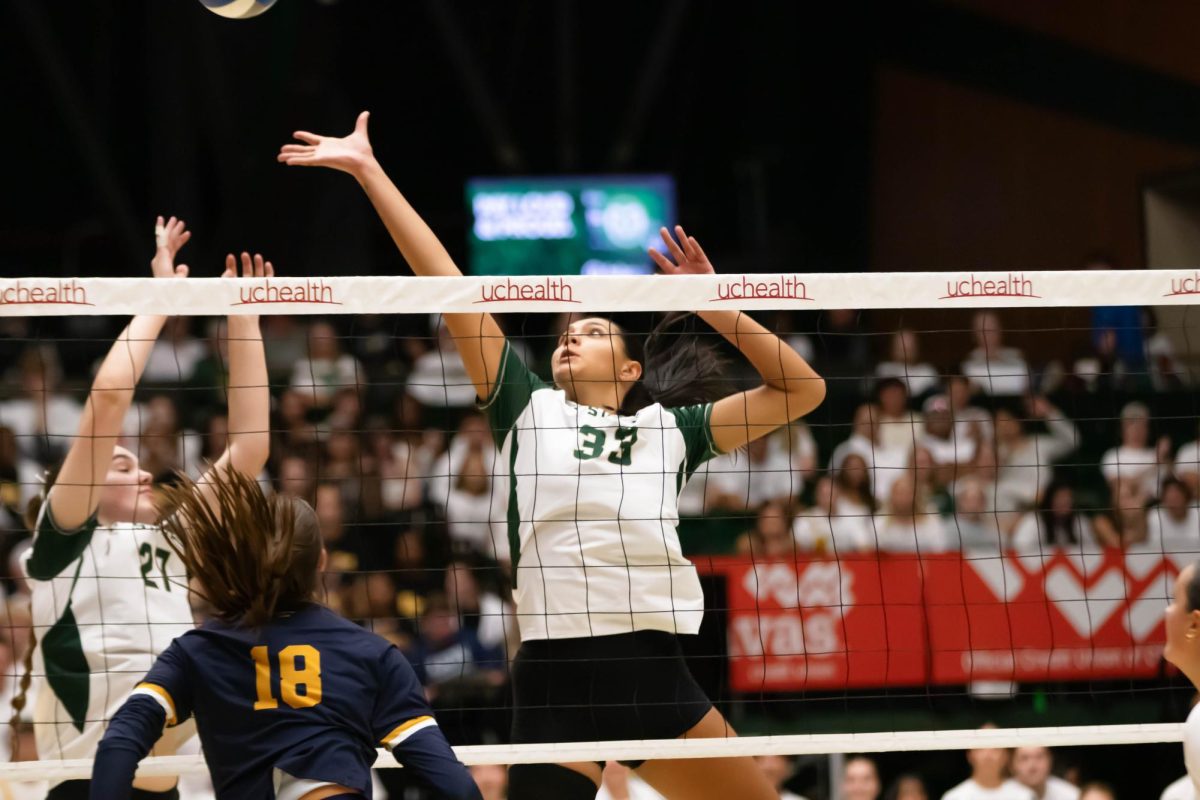 A volleyball player behind a net throws her hand out to hit a volleyball.