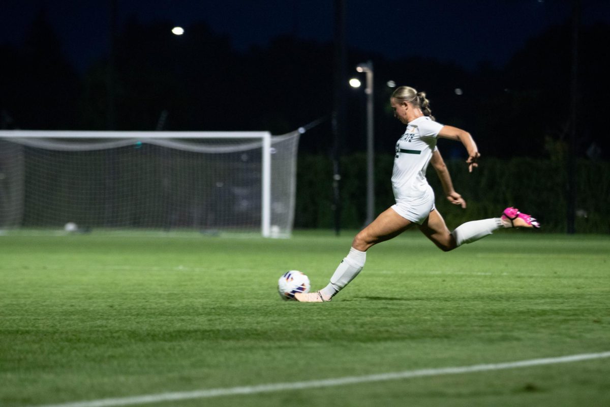 A girl dressed in white kicks a ball on a field.