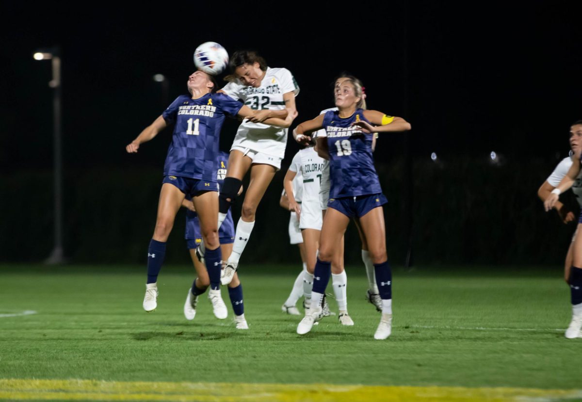 Women in white and blue clothing hits a ball with their heads in a soccer field.