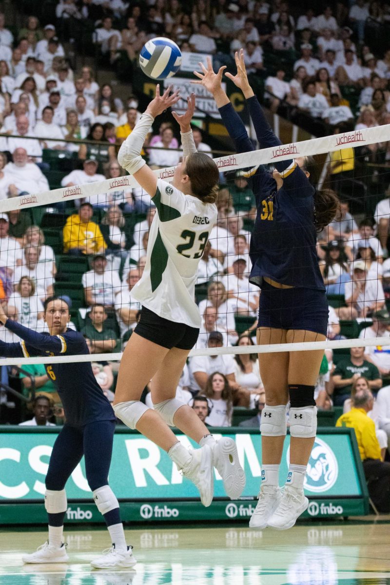 Women's volleyball jumping to set a ball for teammates while opposing team blocks.