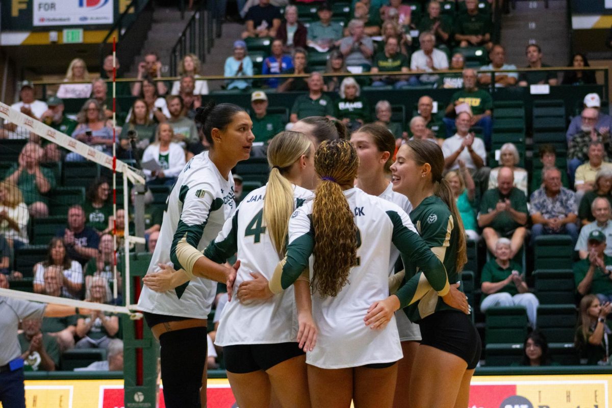 5 women wearing white jerseys and 1 woman wearing a green jersey huddle together.