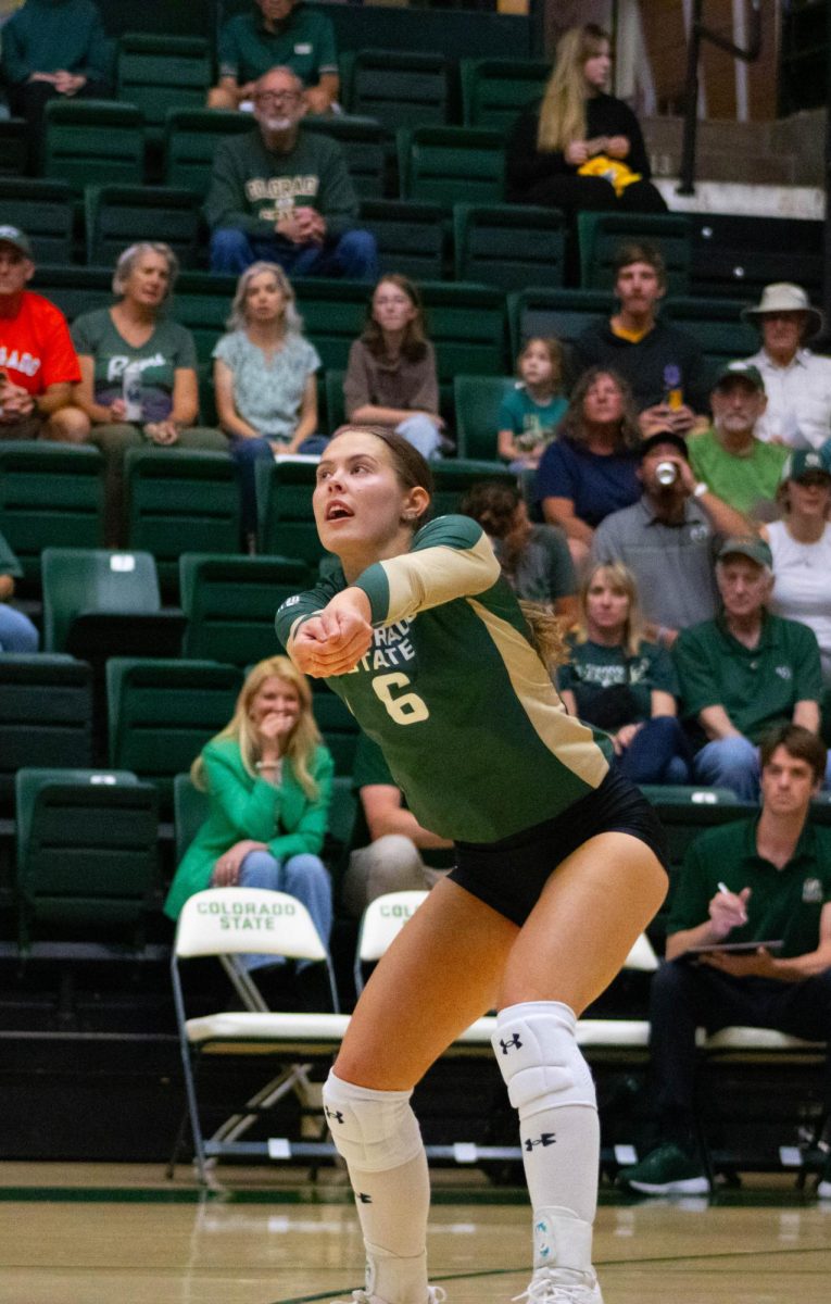 A woman in a green jersey holds her hands out, looking at the ball.
