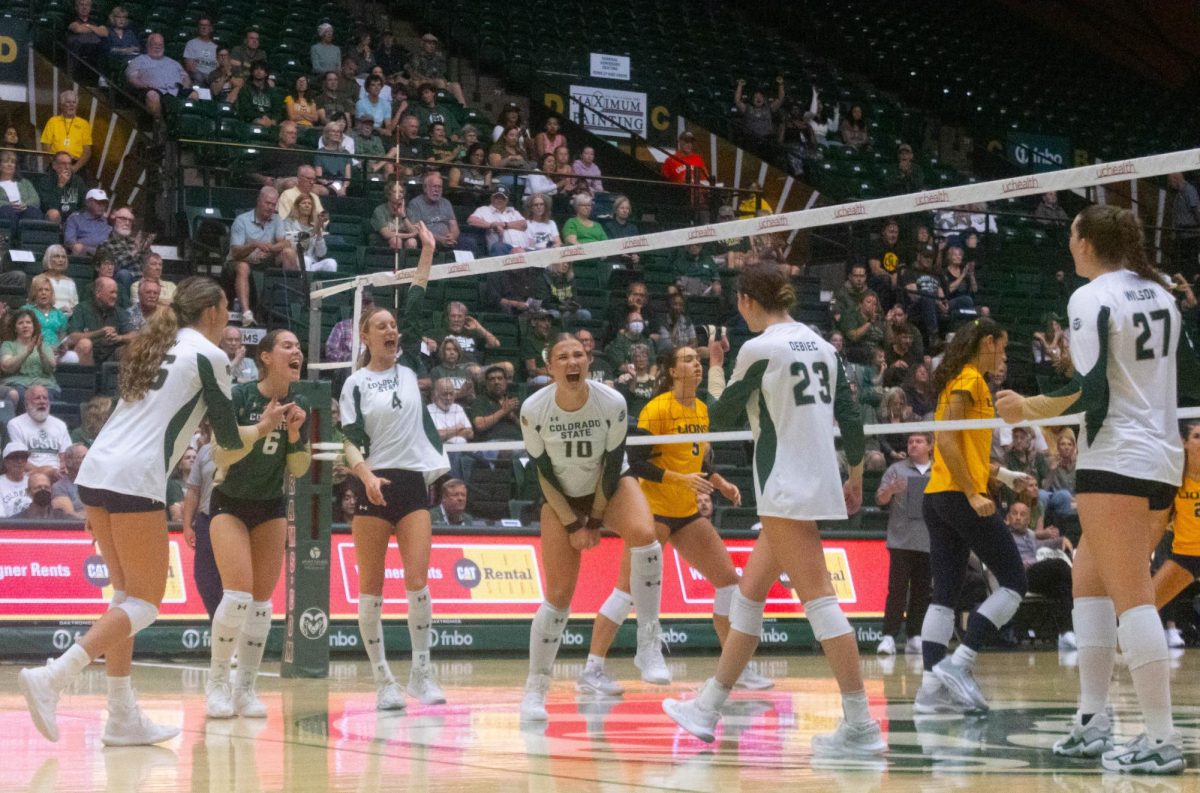 5 women in white jerseys and one woman in a green jersey yelling and clapping together.