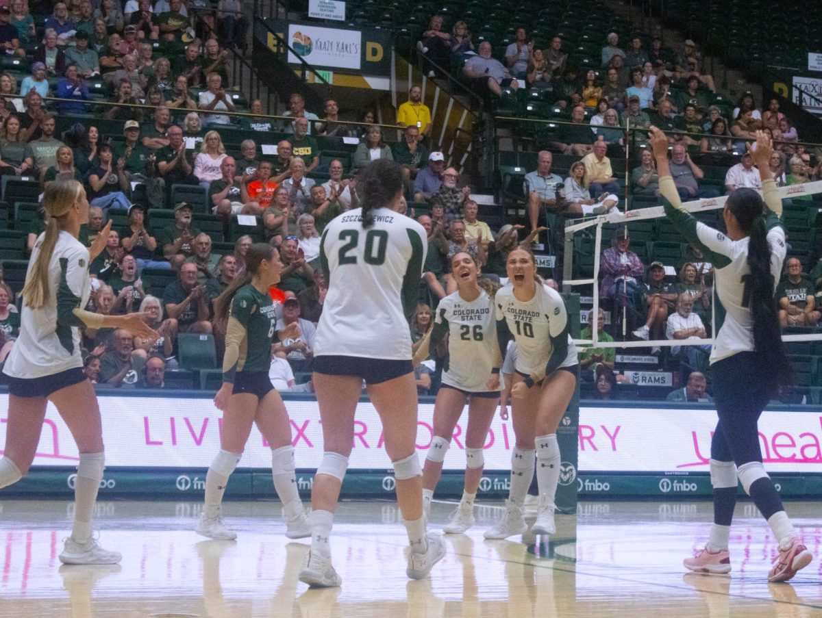 5 women in white jerseys and one women in a green jersey yelling and clapping together.