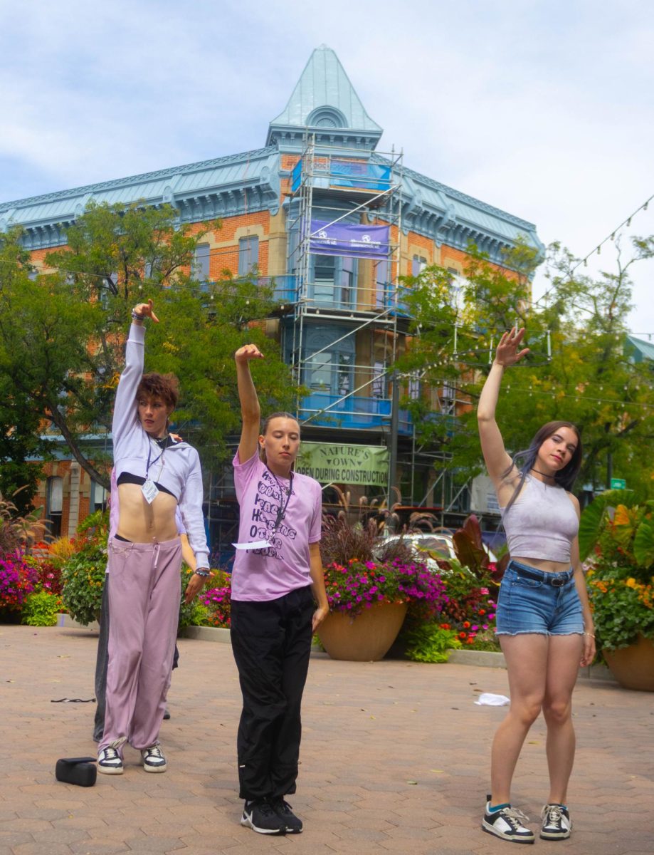 Three hip-hop dancers lined up dancing together. They are all wearing a shade of purple. They are all holding their hands up to finish their performance.