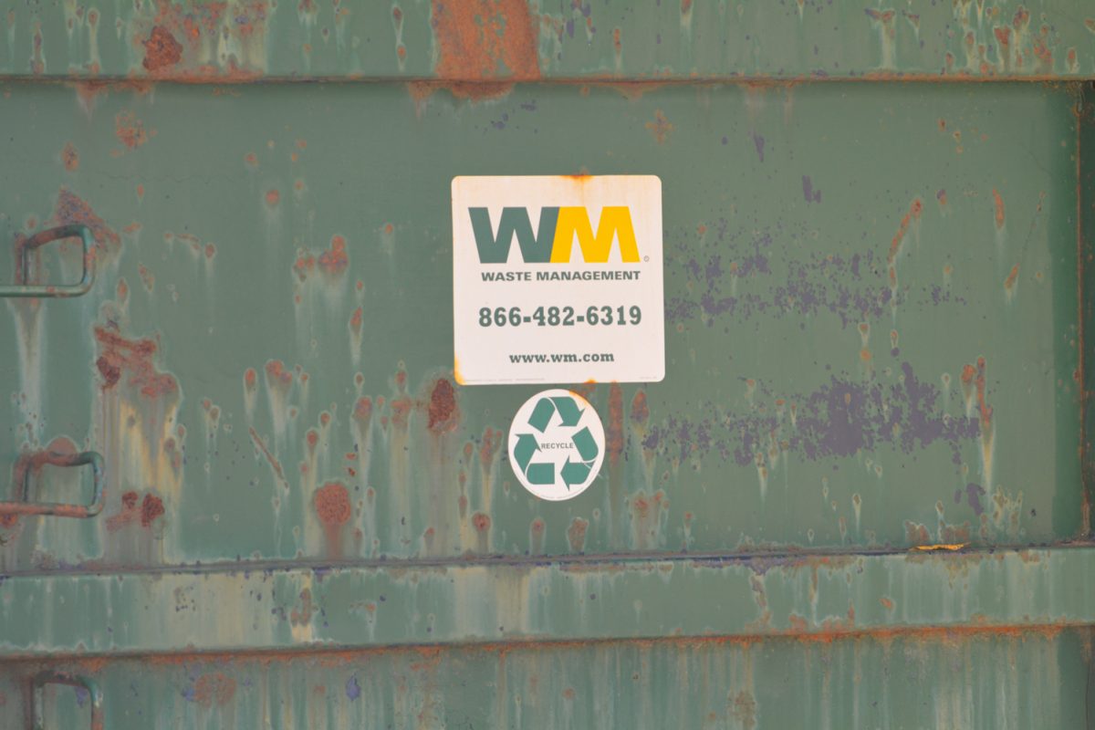 A waste management sign on a green recycling container.