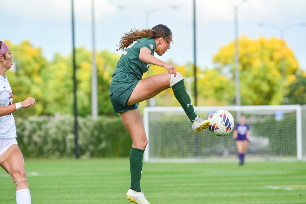 Girl in a green jersey stopping a soccer ball in the air.