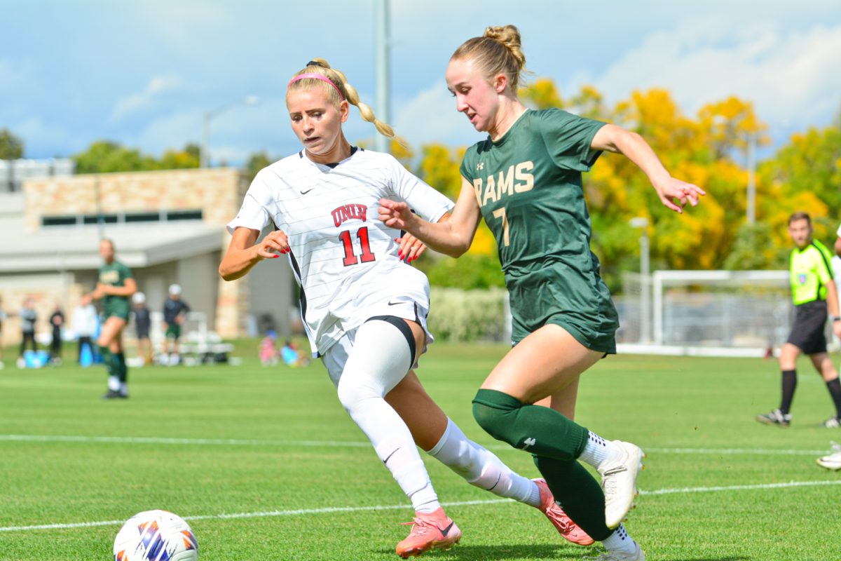 A girl in a green and gold jersey running after the ball.