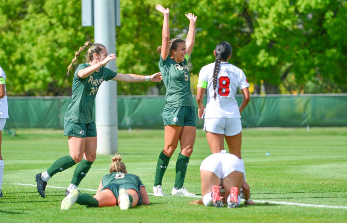 Two girls in a green and gold jersey putting their hands up in celebration.