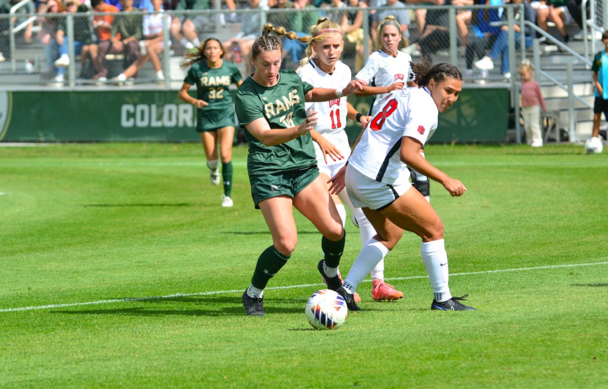 Girl in a green and gold jersey fighting against a girl in a white and red jersey for the ball.