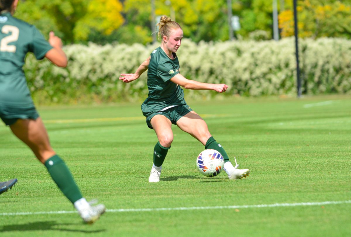 Girl in a green and gold jersey kicking a ball.