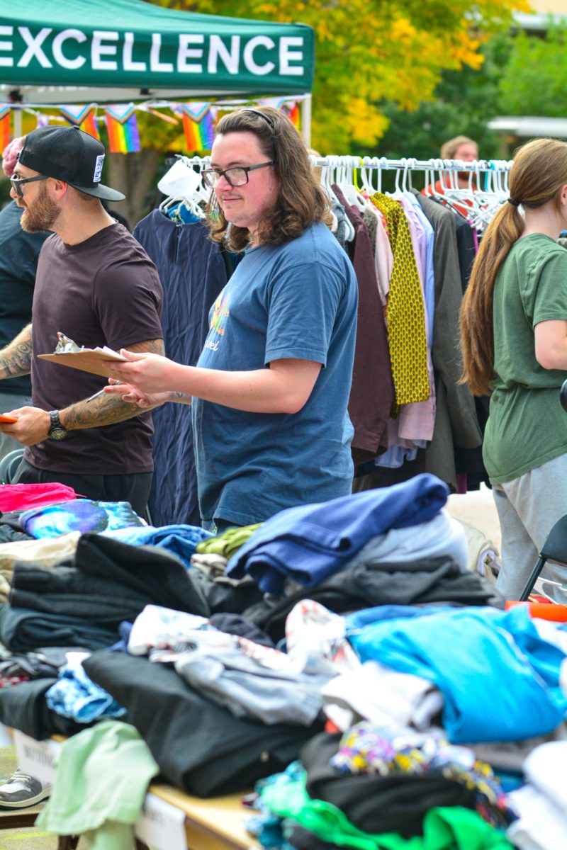 A guy in a blue shirt surrounded by piles of clothing.