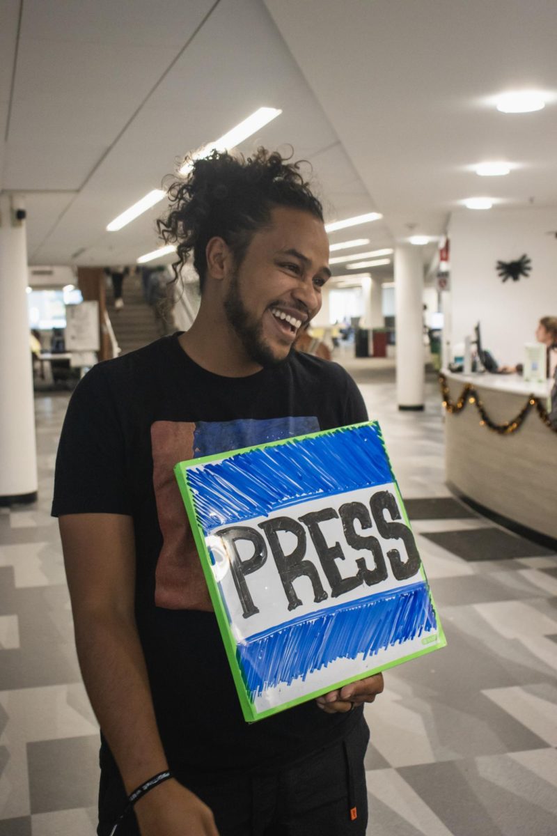 Santino Martinez-Richardson conversing with friends while holding his sign in Morgan Library Oct 6. His goal is not just to display a message, but to inspire others. “What I want from it is to inspire people to do their own actions, to be creative, to use art in their own way,” Martinez-Richardson said.