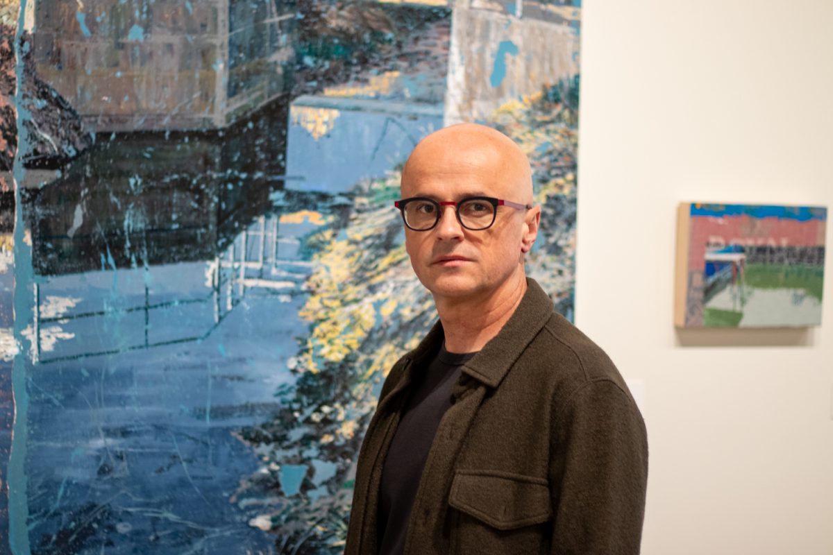 Marius Lehene, a professor of drawing at Colorado State University, stands in front of his painting, “Irrigation Channel,” at the Gregory Allicar Museum of Art Oct. 9. “Where is 'We?'" Lehene said. "Just as impossible to redefine as the chipped, peeling, tired skin of paint, unable to offer immunity to whatever entity it locally and temporarily describes — such is life."
