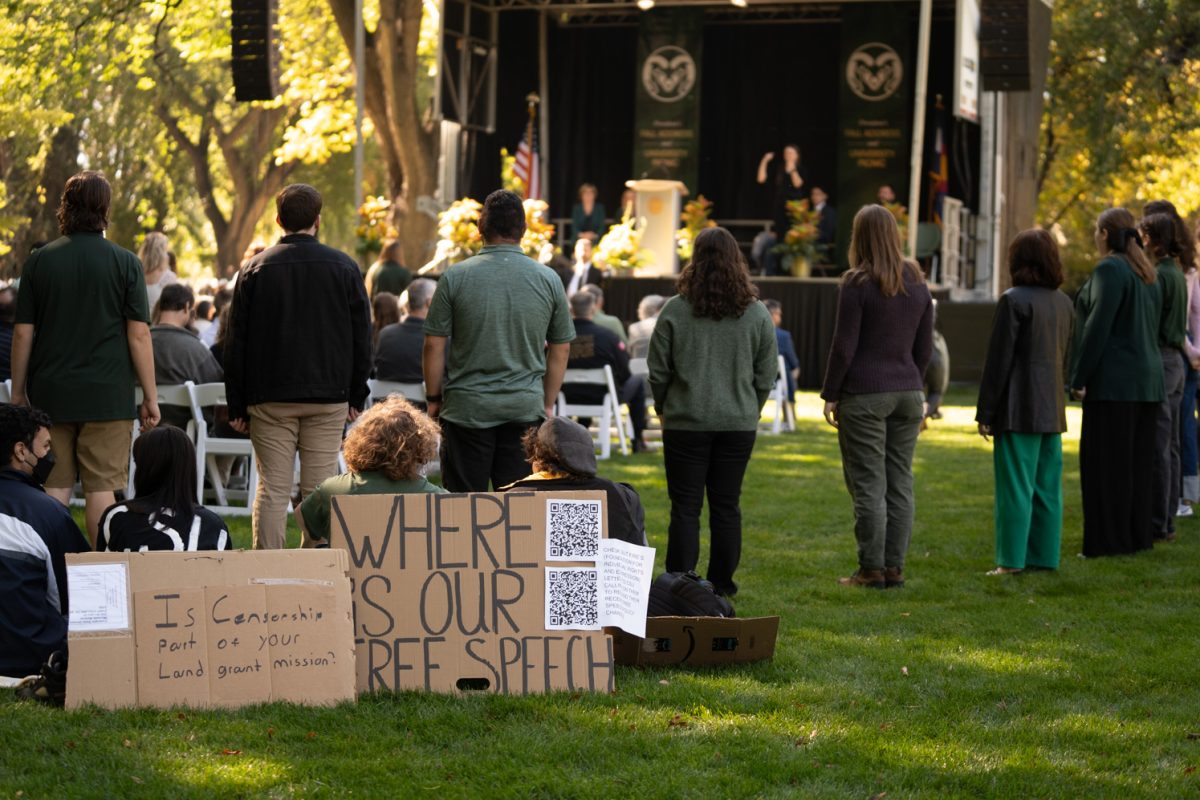 A choir sings in a circle behind protestors sitting on the grass.