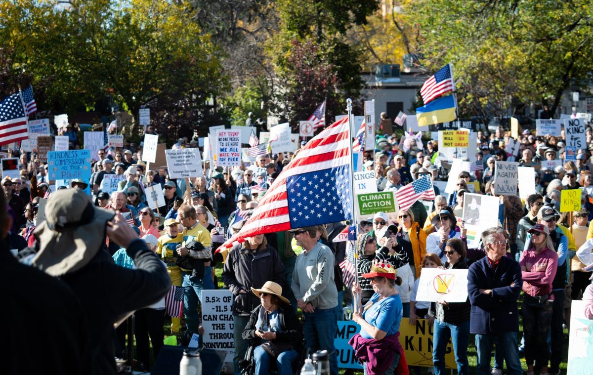 A crowd of protesters gather at a park with signs and flags.