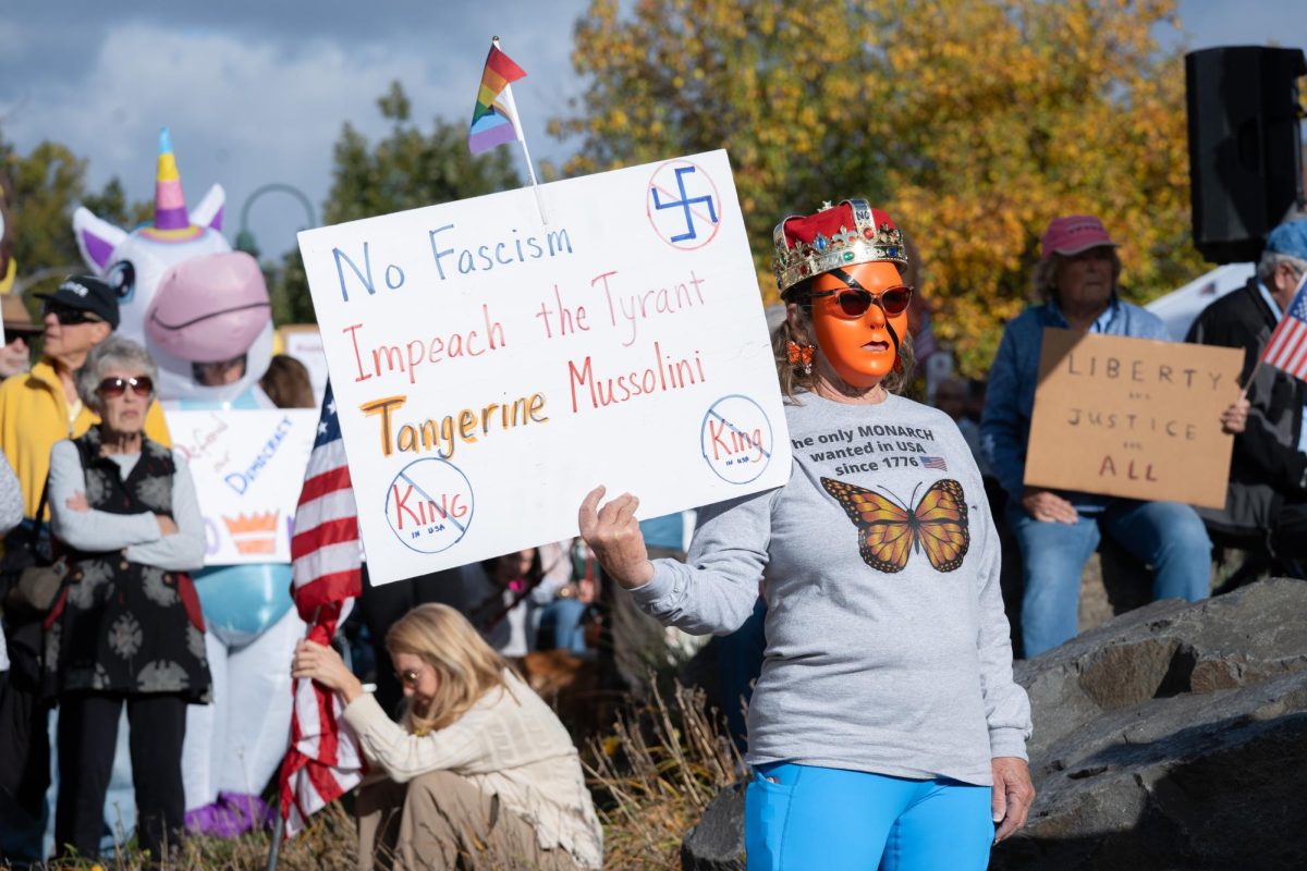 A masked woman holds a sign that reads, "No Fascism, Impeach the Tyrant Tangerine Mussolini."