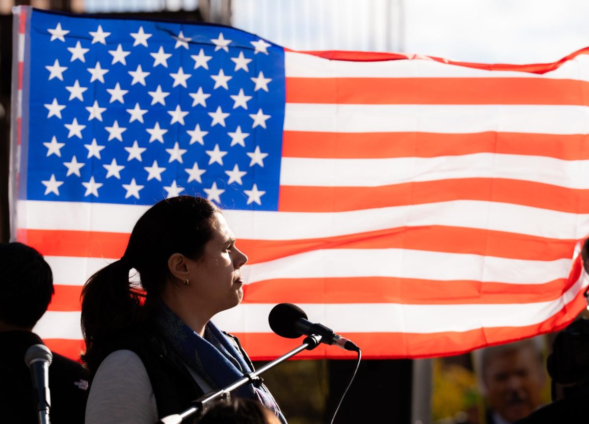 A woman giving a speech in front of the American flag looks into the distance.