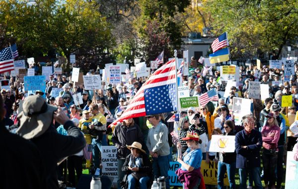 A crowd of protesters gather at a park with signs and flags.