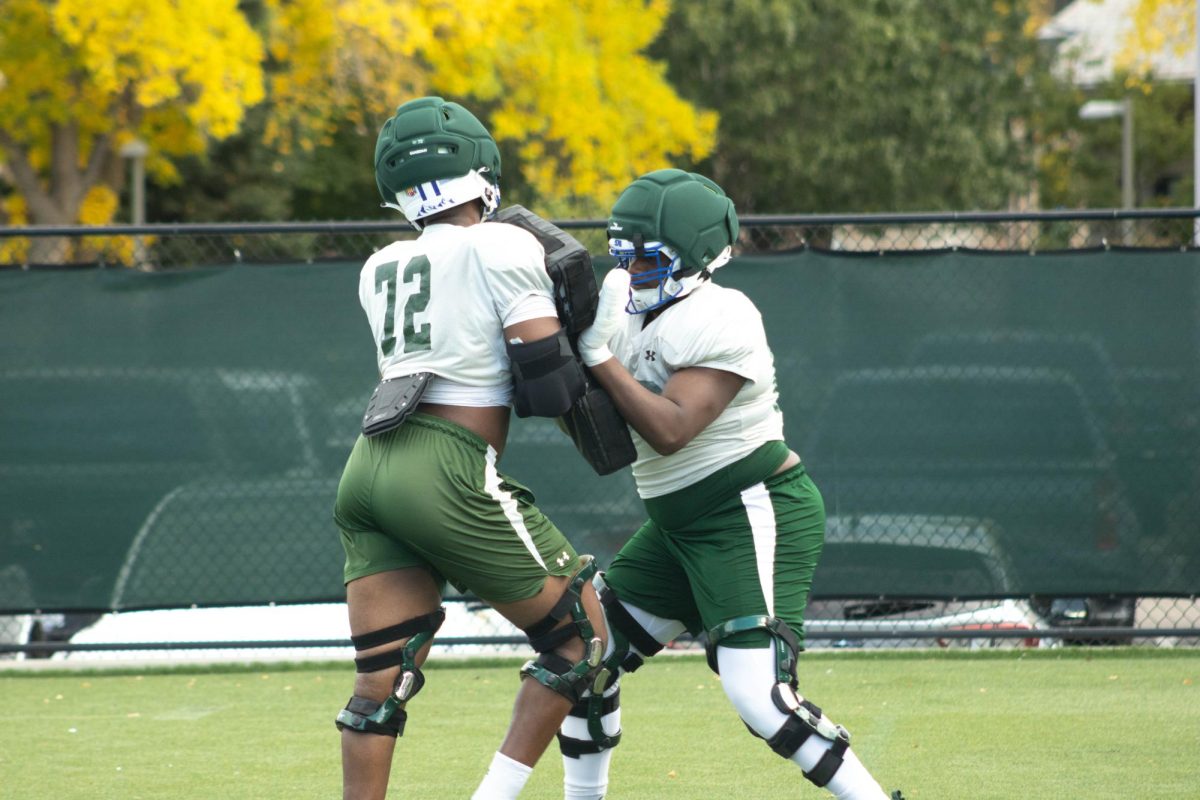 Two players are holding onto each other. One player is holding a padded bag. Both are wearing knee braces on both knees.