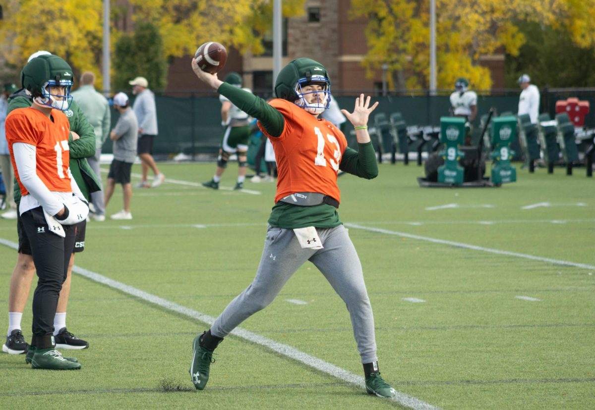 A player wearing an orange jersey has the ball in his right hand, the hand is over his head moving forward.