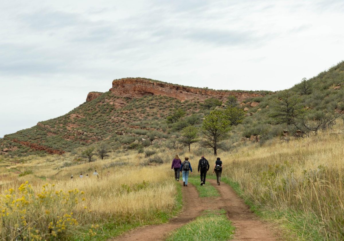 Four people in the middle of a trail with a mountain of red rocks in front of them.