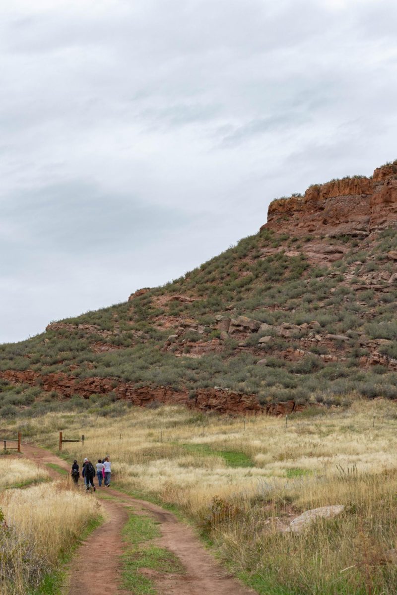 A group of people in the middle of a dirt trail with a mountain of red rocks in front of them to their right.