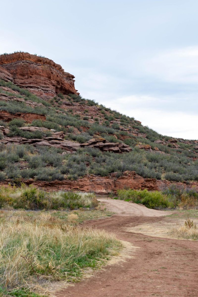 A mountain of red rocks on top of a winding dirt trail below it.