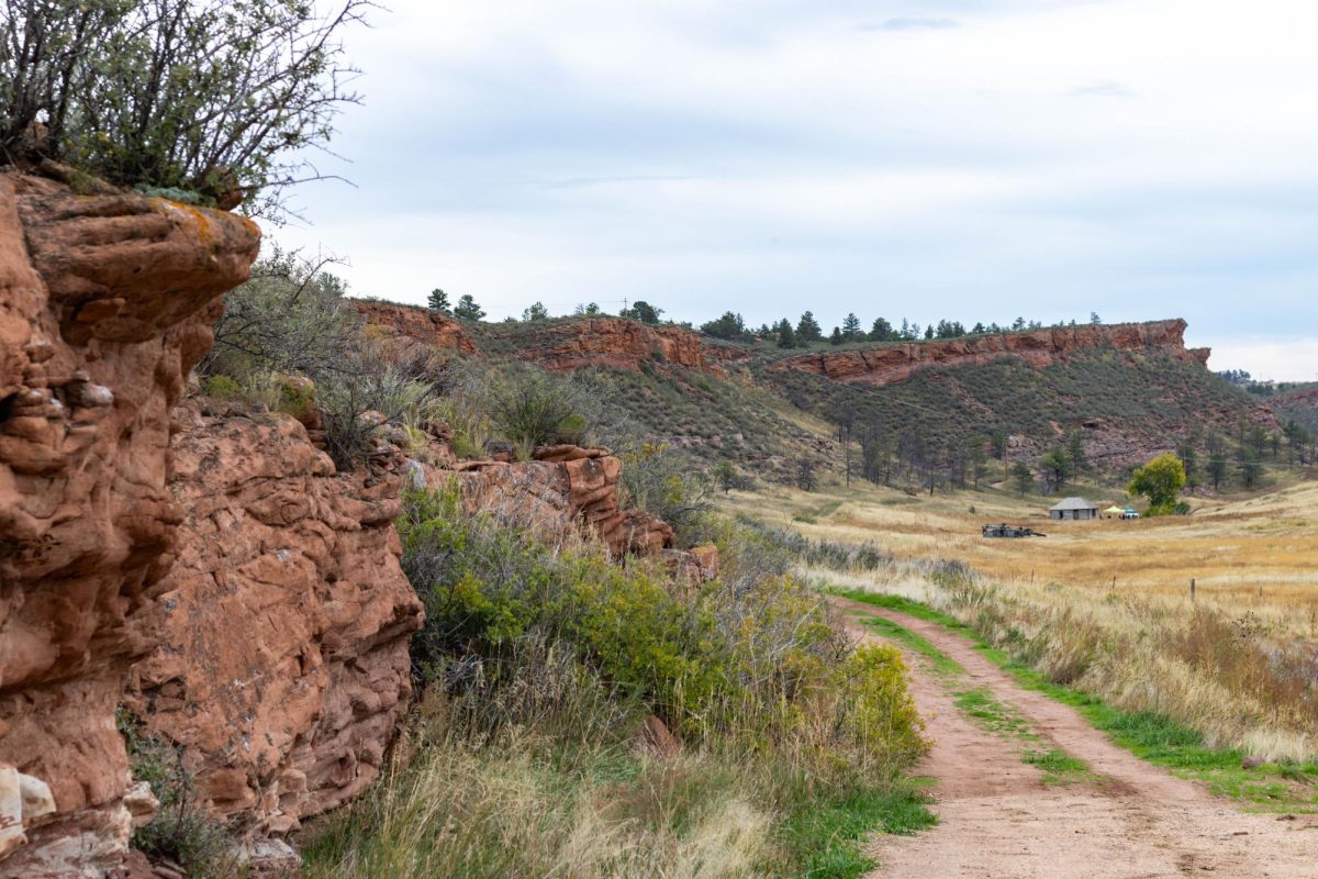 A dirt trail on the right side as there are red rocks framing the trail on the left. There are large red cliffs in the background.