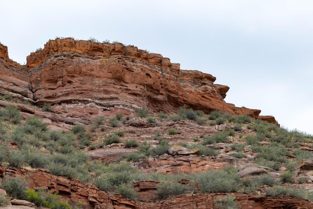 A mountain of red rocks with green shrubs littering it.